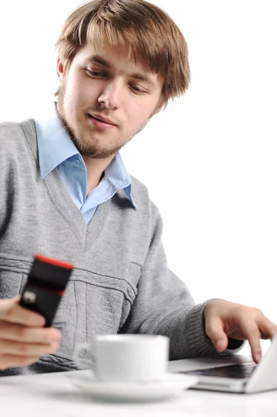 Młody człowiek pisania krótkich wiadomości na telefon komórkowy, pracuje na laptopie i pić — Zdjęcie stockowe