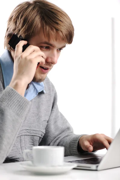 Hombre joven hablando en el teléfono celular y trabajando en el portátil — Foto de Stock