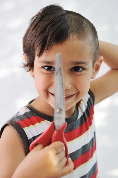 Niño cortar el pelo a sí mismo con tijeras, mirada divertida — Foto de Stock