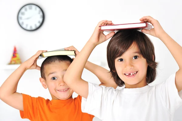 Felices chicos lindos en casa, adorables hermanitos con libros sobre cabezas —  Fotos de Stock