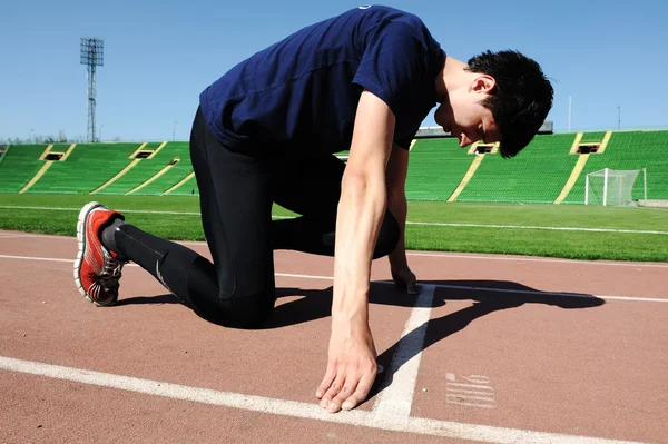 Молодой спортсмен находится в начале беговой дорожки на стадионе — стоковое фото