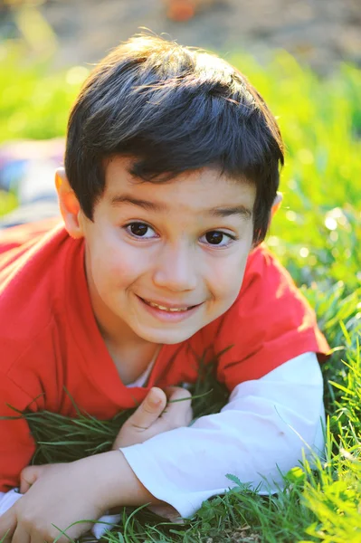Petit garçon mignon étendu sur l'herbe d'été du matin avec une belle lumière naturelle — Photo