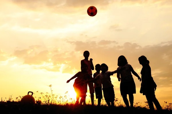 Silueta, grupo de niños felices jugando en el prado, puesta de sol, verano —  Fotos de Stock