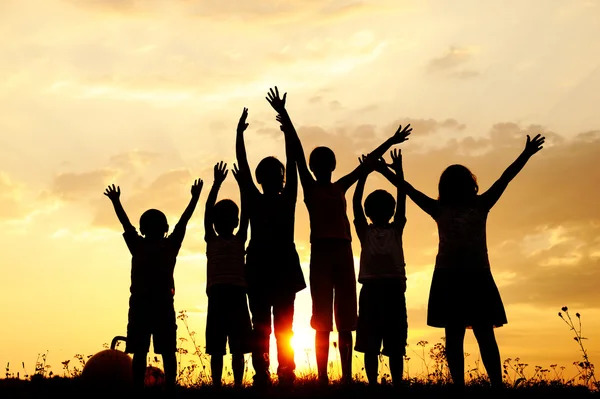 Silhouette, Gruppe fröhlicher Kinder, die auf der Wiese spielen, Sonnenuntergang, Sommer — Stockfoto