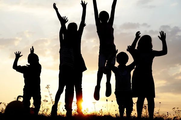 Silueta, grupo de niños felices jugando en el prado, puesta de sol, verano —  Fotos de Stock