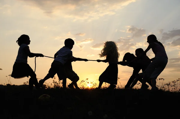 Sziluettjét, játszik a rét, a naplemente, a nyári boldog gyermekek csoportja — Stock Fotó