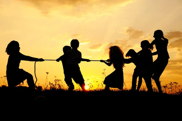Силуэт, группа счастливых детей, играющих на лугу, закат, лето — стоковое фото