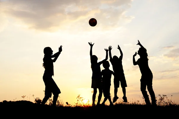 Silhouet, groep van gelukkige kinderen spelen op de weide, zonsondergang, 's zomers — Stockfoto