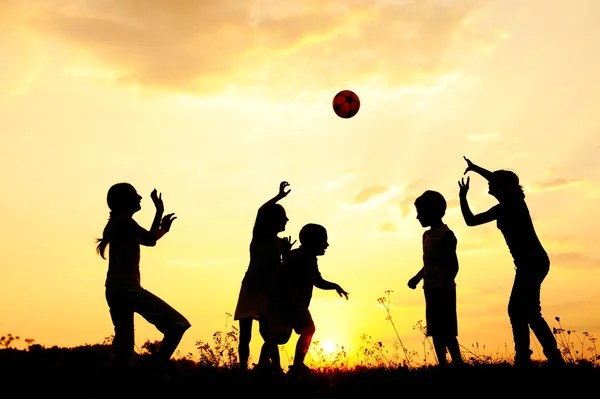 Σιλουέτα, ομάδα χαρούμενα παιδιά να παίζουν σε Λιβάδι, ηλιοβασίλεμα, καλοκαίρι — Φωτογραφία Αρχείου
