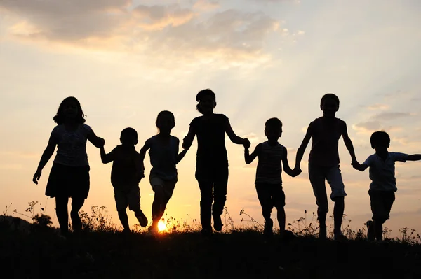 Silhouette, Gruppe fröhlicher Kinder, die auf der Wiese spielen, Sonnenuntergang, Sommer — Stockfoto