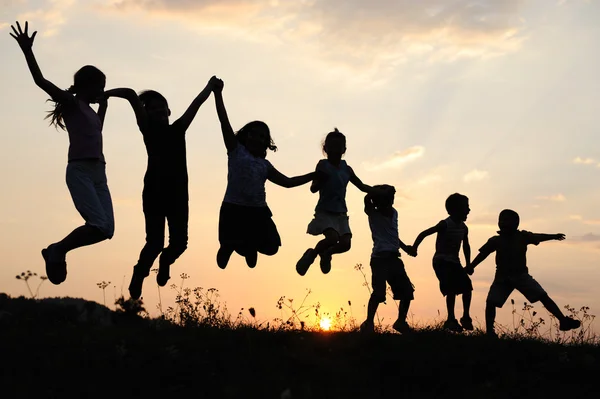 Silhouette, Gruppe fröhlicher Kinder, die auf der Wiese spielen, Sonnenuntergang, Sommer — Stockfoto