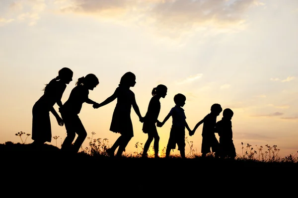 Silueta, grupo de niños felices jugando en el prado, puesta de sol, verano — Foto de Stock