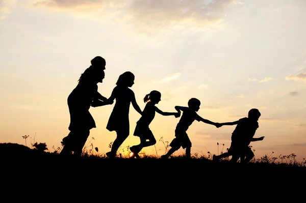 Silhouette, group of happy children playing on meadow, sunset, summertime — Stock Photo, Image