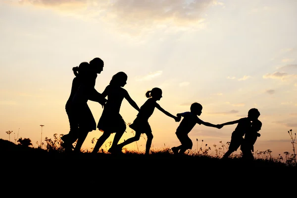 Silhouette, grupp av glada barn spelar på ängen, solnedgång, sommartid — Stockfoto
