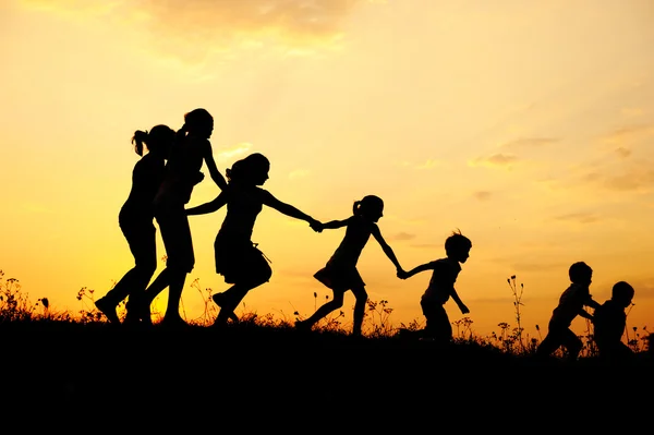 Silhouette, groupe d'enfants heureux jouant sur prairie, coucher de soleil, été — Photo