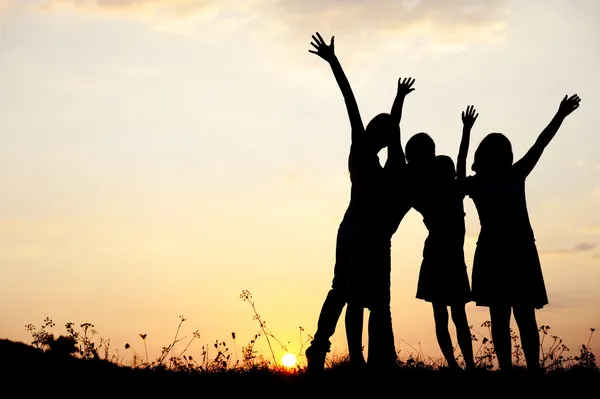 Silueta, skupina šťastných dětí hraje na louce, západ slunce, léto — Stock fotografie