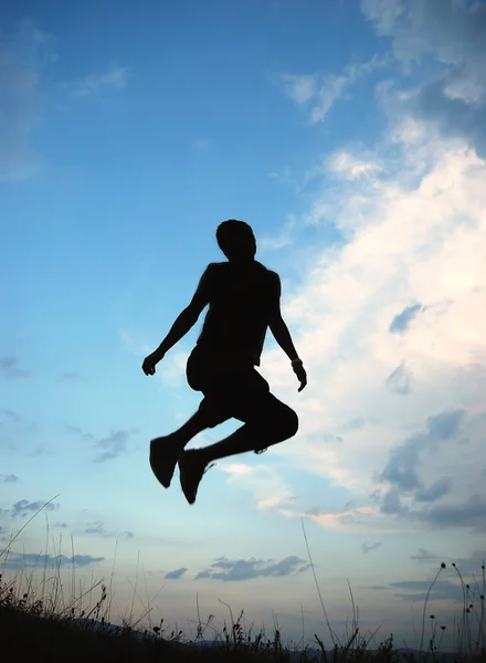 Νέοι ευτυχισμένος άνθρωπος πηδά στον πράσινο λιβάδι, σιλουέτα — Φωτογραφία Αρχείου