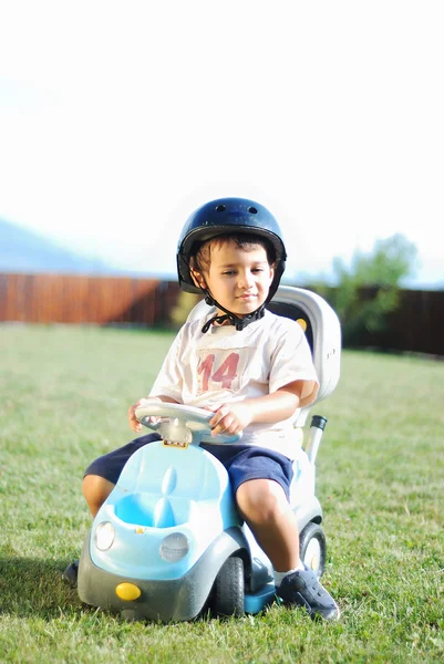 Criança no prado verde dirigindo um carro de brincar — Fotografia de Stock