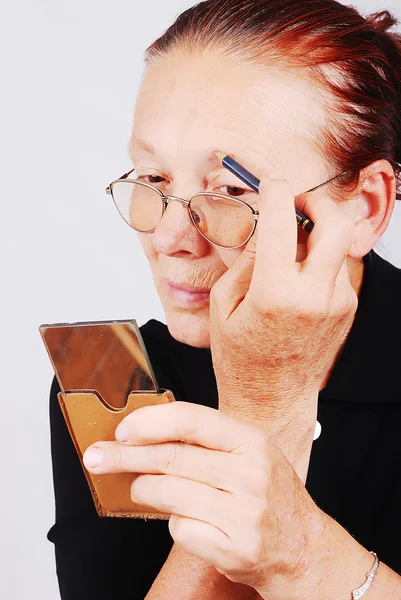 Mulher idosa colocando maquiagem no rosto — Fotografia de Stock