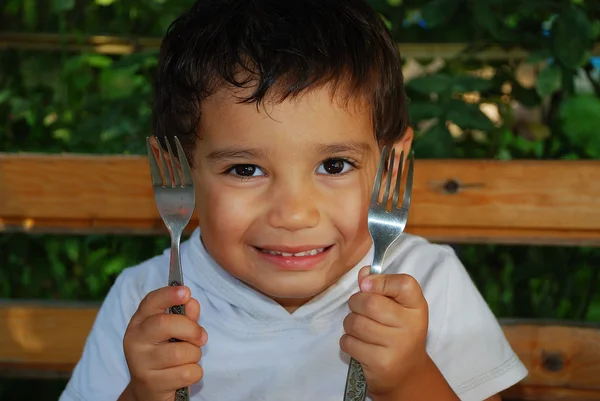 Pequeno menino bonito está segurando colher e garfo — Fotografia de Stock