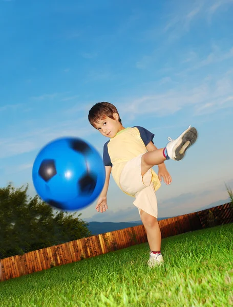Pequeno garoto bonito está batendo bola por seu pé — Fotografia de Stock