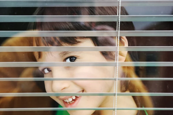 Πορτρέτο του ένα αθώο μικρό αγόρι που κρυφοκοιτάζει μέσα από το παράθυρο με περσίδες Royalty Free Φωτογραφίες Αρχείου