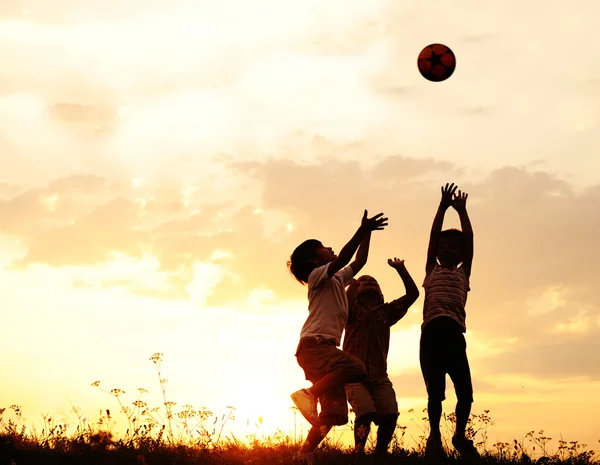 Silueta, grupo de niños felices jugando en el prado, puesta de sol, verano Imagen de archivo