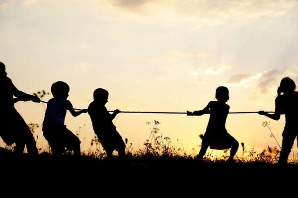 Силует, Група щасливих дітей, що грають на луг, захід сонця, літній час Ліцензійні Стокові Зображення