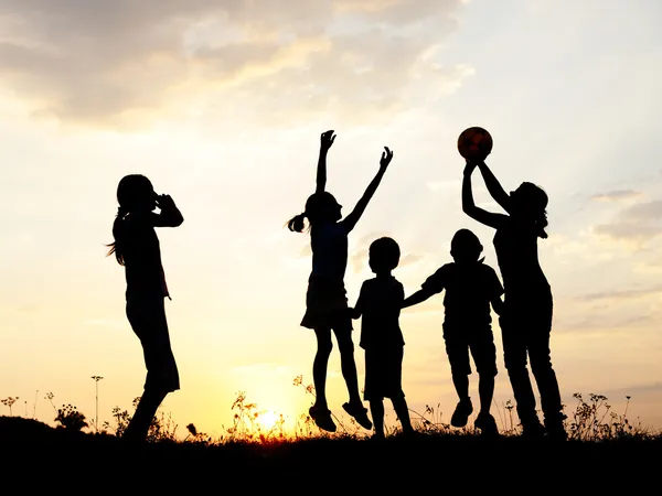 Silhouette, gruppo di bambini felici che giocano sul prato, tramonto, estate Immagine Stock
