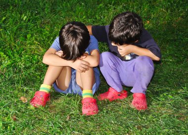 Two cute children sitting on ground, consoling each other clipart