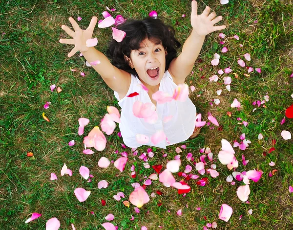 Menina bonita feliz no chão com pétalas de rosa — Fotografia de Stock