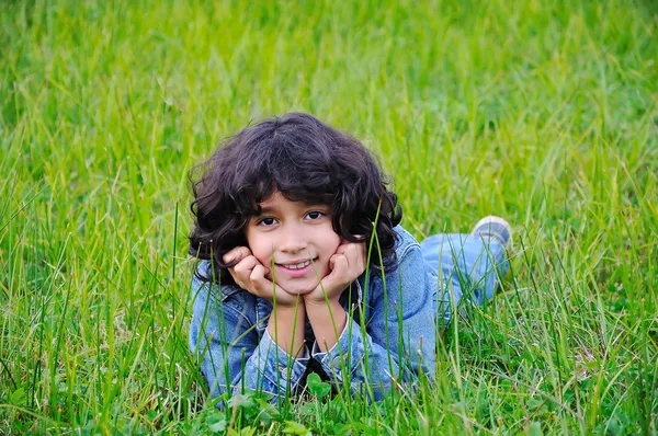 Une petite fille heureuse et mignonne allongée sur le sol vert — Photo