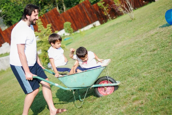 Dad in white driving boys on the wheelbarrow — Stock Photo, Image