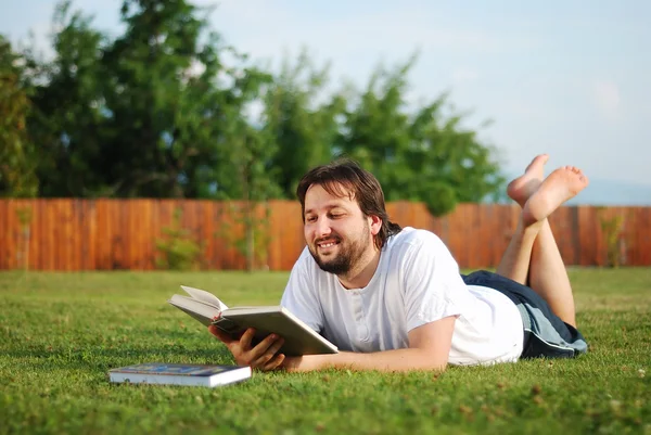 Giovane uomo è sdraiato su un terreno verde e di apprendimento — Foto Stock