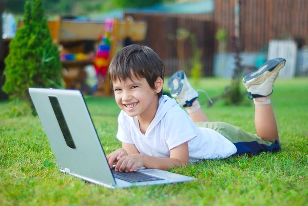 Cute kid is laying on laptop in beautiful environment — Stock Photo, Image