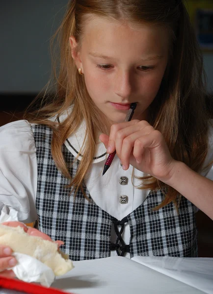 Kleines süßes Mädchen im Klassenzimmer, beim Schreiben und Essen — Stockfoto