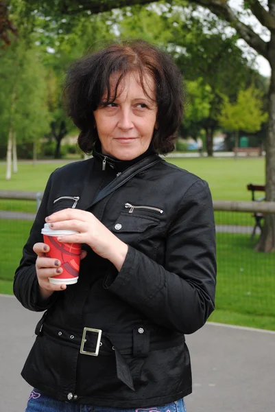 Volwassen vrouw koffie drinken in het park — Stockfoto