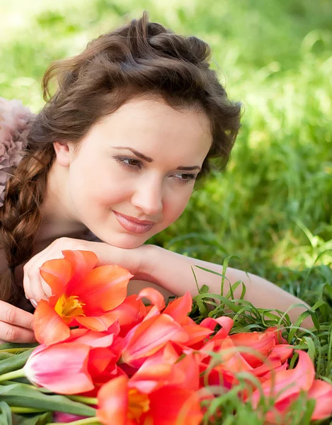 Vacker kvinna med röda fjädrar tulpaner i en trädgård — Stockfoto