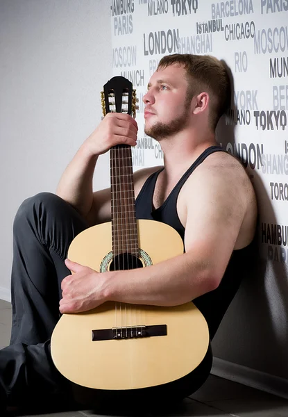 Молодой человек с гитарой на темном фоне — стоковое фото