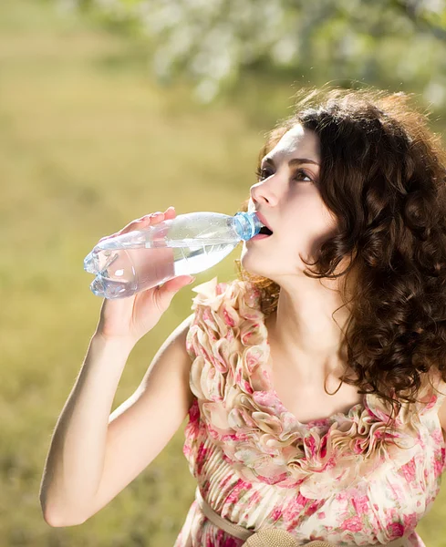 Beautiful woman drinks cold water in spring garden — Stock Photo, Image