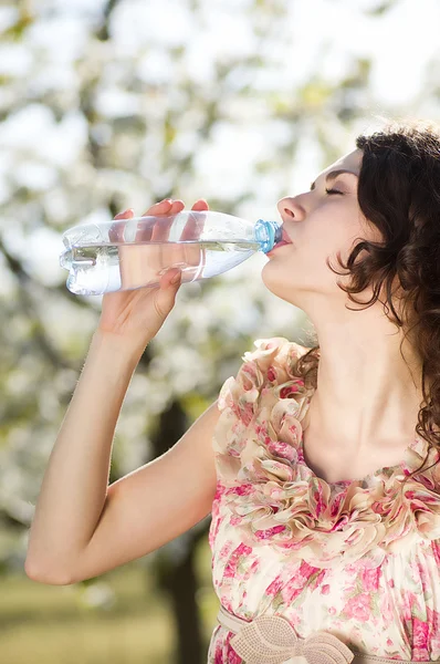Beautiful woman drinks cold water in spring garden — Stock Photo, Image