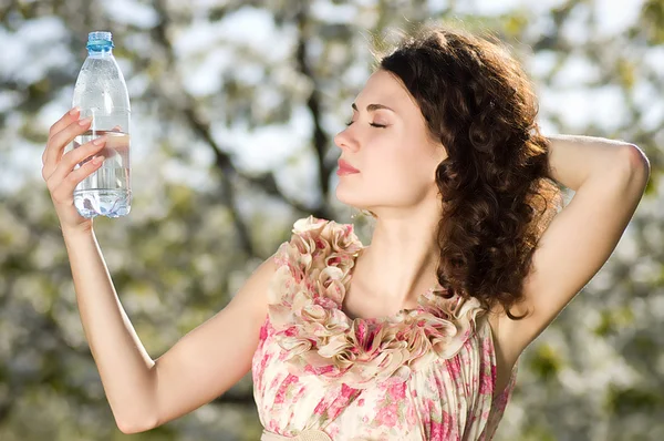 Vacker kvinna dricker kallt vatten i vårträdgård — Stockfoto