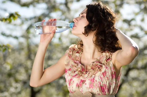 Mooie vrouw koud water drinkt in lentetuin — Stockfoto