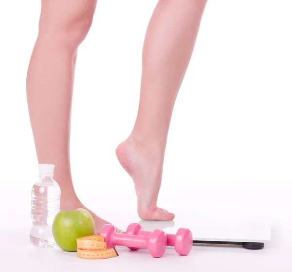 Kvinnliga fötterna på skalor med mått, äpple, tyngdlyftningsvikter — Stockfoto