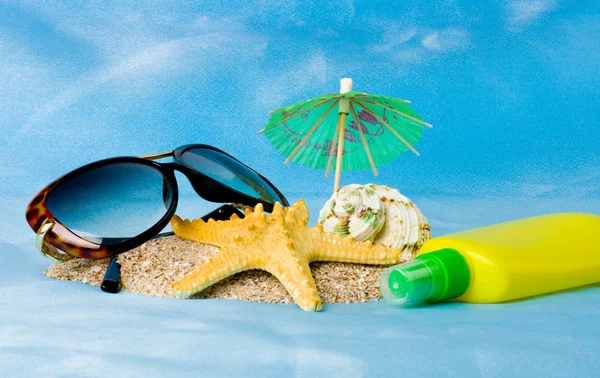 Раковина, очки, морская звезда и крем для загара на песке — стоковое фото