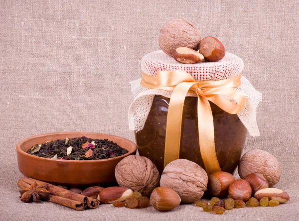 Smakelijke jam, cupcakes, klei pot en noten op achtergrond — Stockfoto