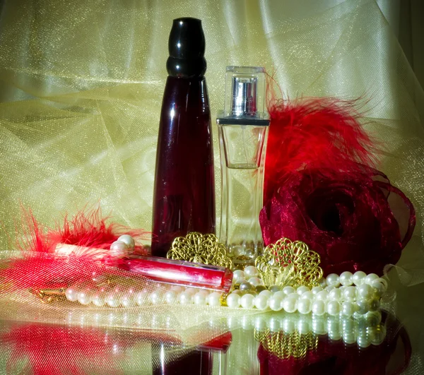 Парфюмерные бутылки, красная помада, перо, бусы из роз и жемчуга — стоковое фото