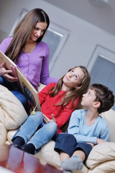 Молодая мама играет со своими детьми дома и читает книги — стоковое фото
