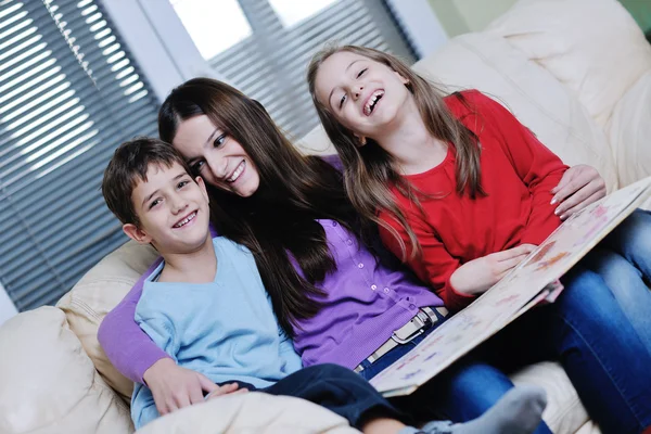 Junge Mutter spielt mit ihren Kindern zu Hause und liest Buch — Stockfoto
