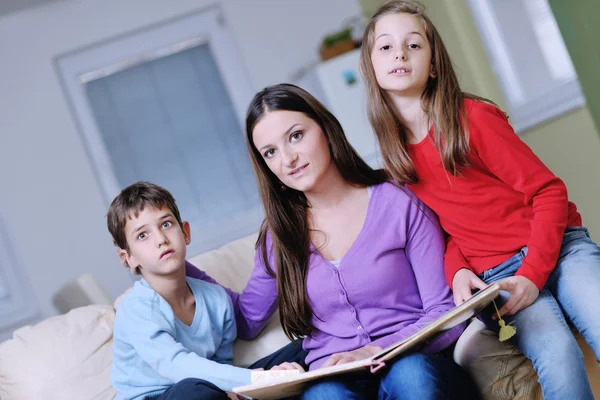 Junge Mutter spielt mit ihren Kindern zu Hause und liest Buch — Stockfoto